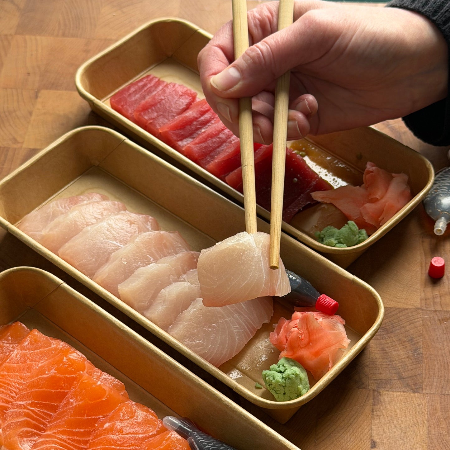 Three trays of sashimi on a wooden surface