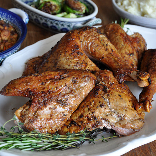 Roasted turkey parts served on a large white platter with garnish, surrounded by side dishes on a wooden table.