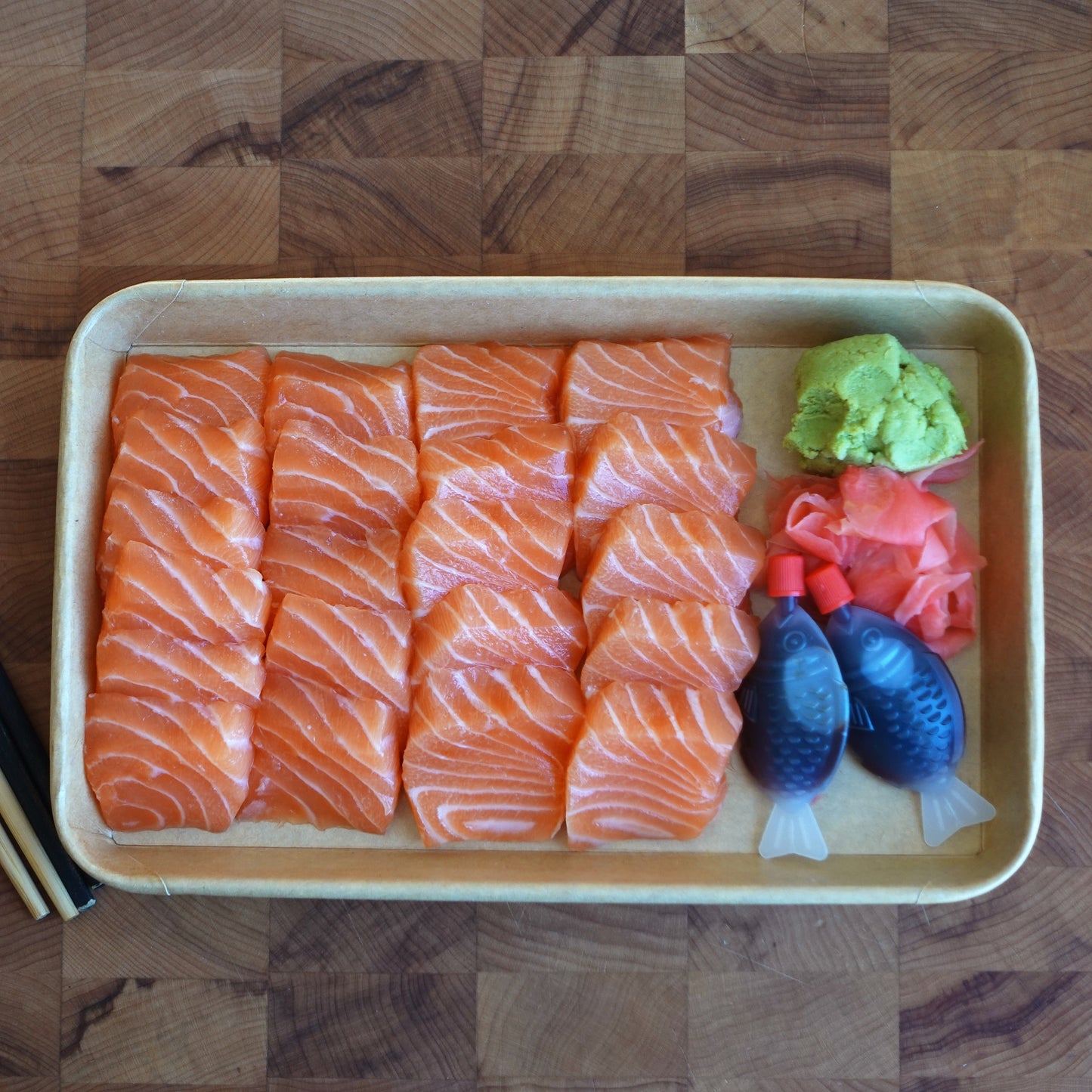 Platter of raw salmon sashimi with wasabi and ginger on a wooden surface.