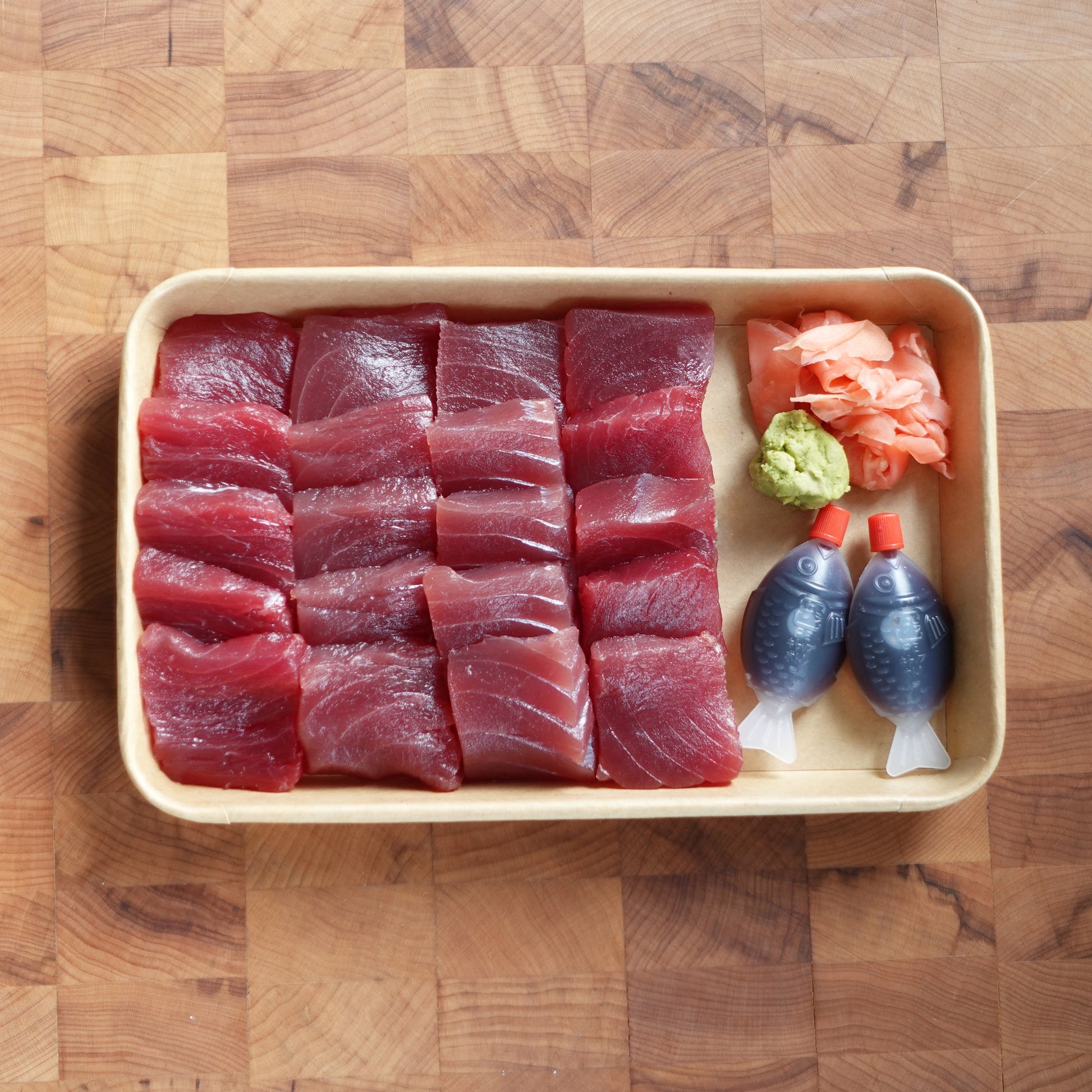 Raw fish slices in a tray with wasabi and soy sauce on a wooden surface