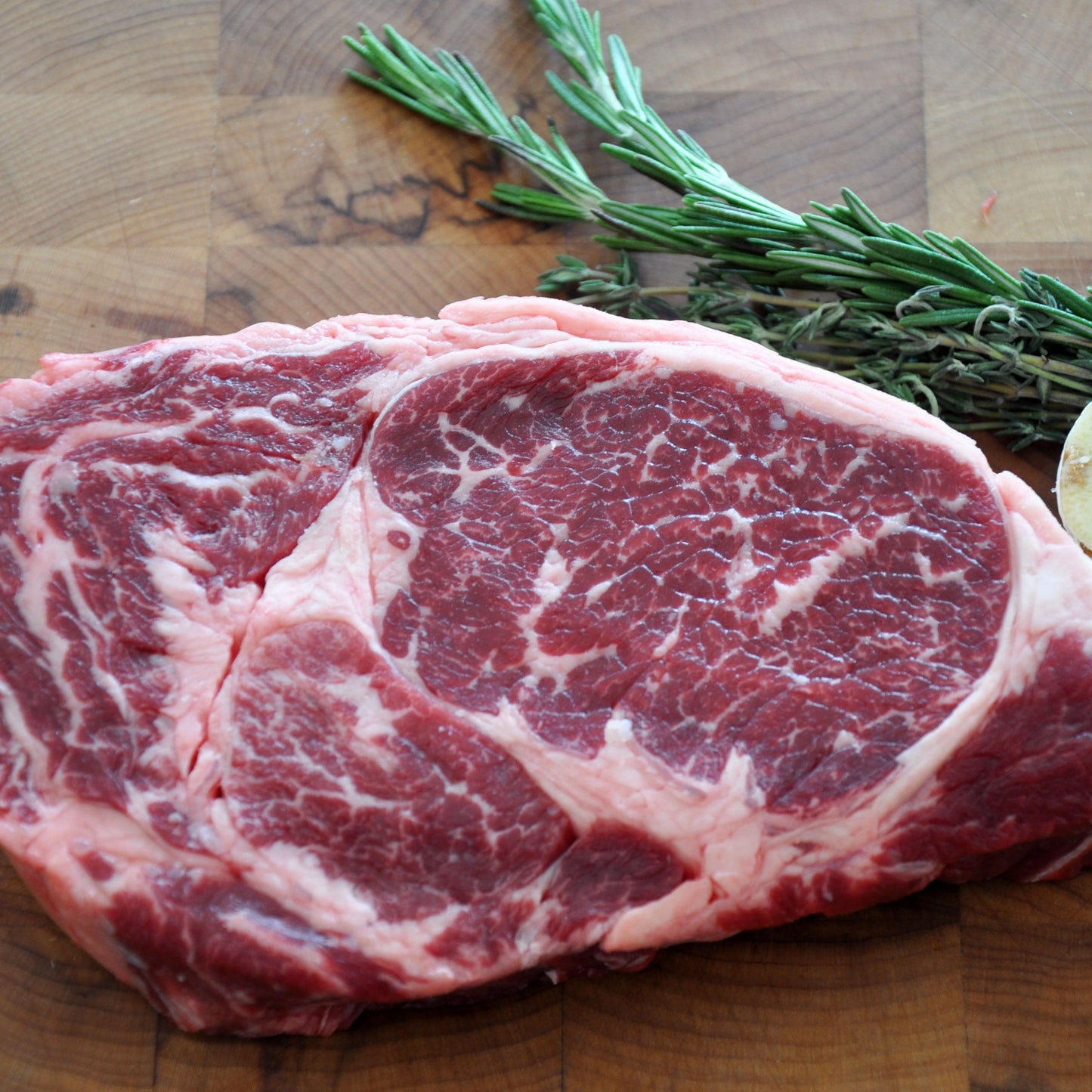 A close up of a boneless ribeye next to herbs on top of a wooden board.