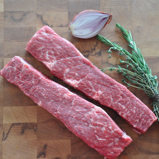 Medium shot of raw prime Denver steaks next to fresh vegetables on a wooden board.
