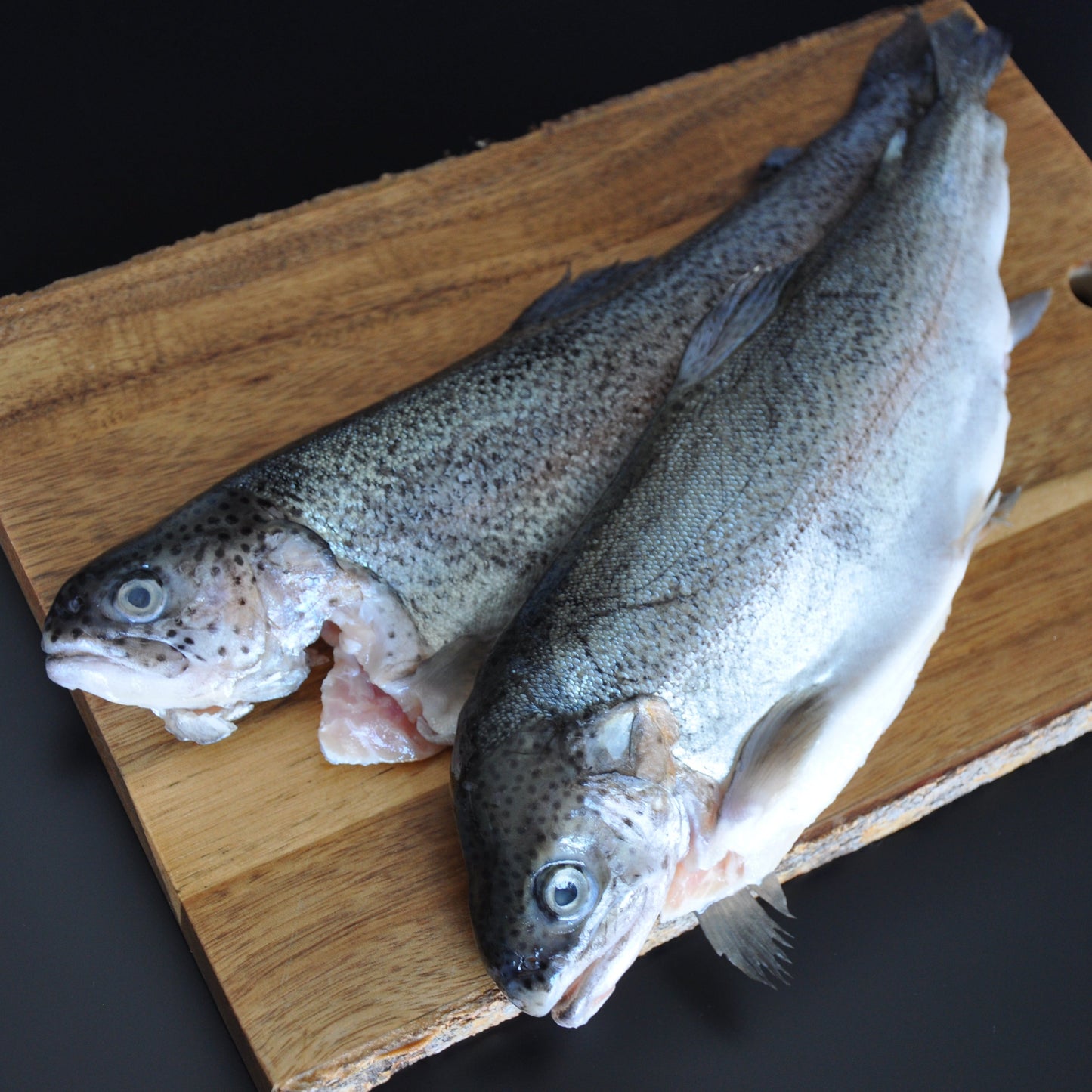 Two raw rainbow trout fish on a wooden board
