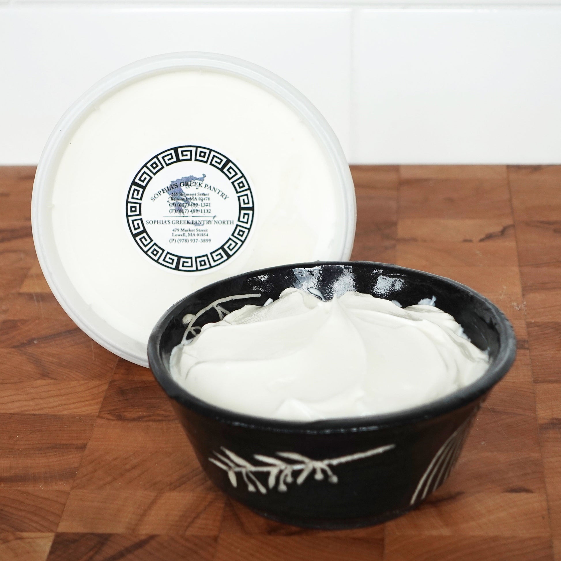 A black bowl with yogurt next to a yogurt container on a wooden board