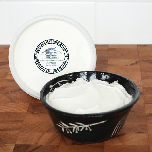 A black bowl with yogurt next to a yogurt container on a wooden board