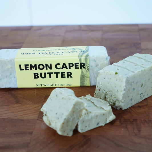 Two butter sticks on a wooden board. The label reads "lemon caper butter"