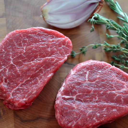 Medium shot of two cuts of raw prime filet mignon on top of a wooden board.