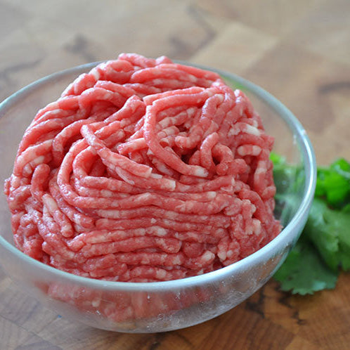 Freshly grounded meat in a bowl next to cilantro leaves.