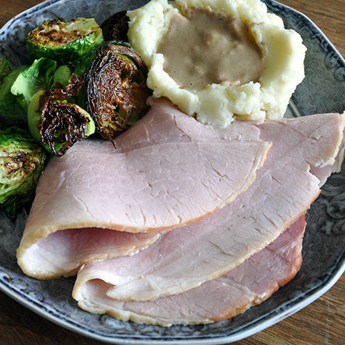 smoked ham sliced on a plate with mashed potatoes and brussel sprouts